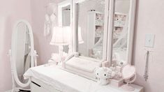 a white dresser topped with a baby crib next to a mirror and teddy bear