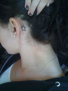 a woman with a star tattoo on her neck and behind her ear is looking down at the ground