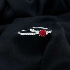 two white gold rings with a red stone in the middle on a black cloth background