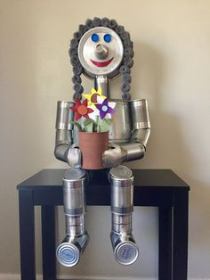 a metal robot holding a flower pot on top of a table