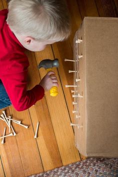 a young boy playing with wooden pegs on the floor next to a cardboard box