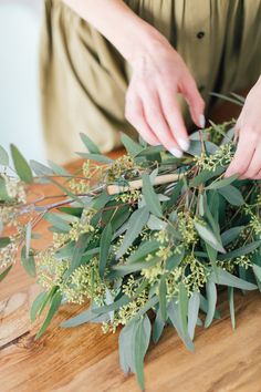 a woman is arranging greenery on top of a wooden table with her hands touching the stems