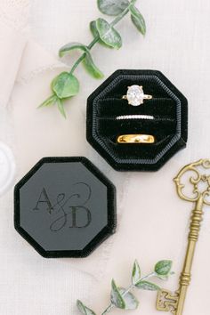 two wedding rings are sitting on top of a black ring box and next to a key