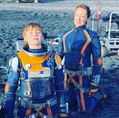 two young boys in space suits sitting on the ground next to each other with their eyes closed