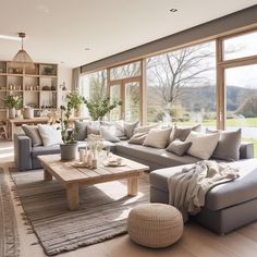 a living room filled with lots of furniture and large windows overlooking a field in the distance