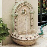 a water fountain sitting on the side of a building next to a potted plant