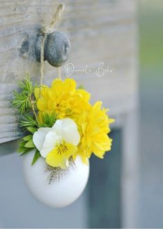 a white vase with yellow and white flowers hanging from the side of a wooden door