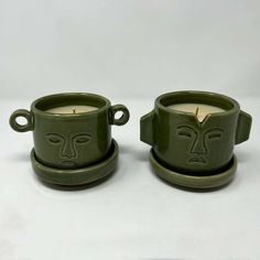 two green cups with faces on them sitting next to each other, one has a candle in it