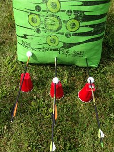 four red cups are lined up in front of a green bag with golf tees on it