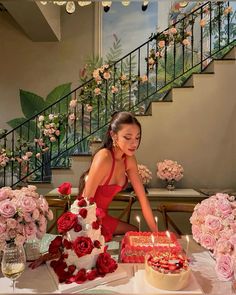 a woman sitting at a table with a cake in front of her and pink flowers