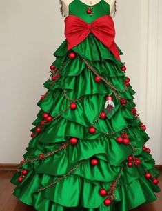 a green christmas tree with red ornaments and bows on it's neck, in front of a white wall