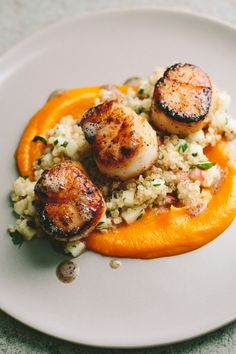 some scallops are on top of rice and carrots in a white plate