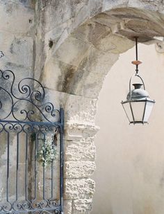 an iron gate with a light hanging from it's side next to a stone wall