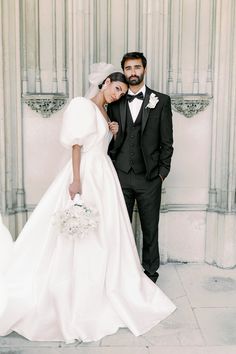 a bride and groom pose for a photo in front of an ornate wall with columns