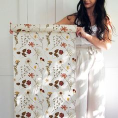 a woman holding up a floral print curtain