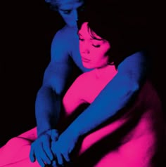 a man and woman sitting next to each other on a bed with pink and blue colors