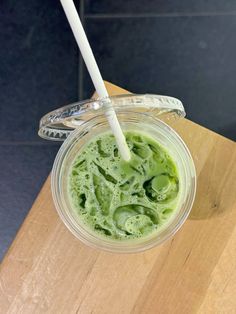 a cup filled with green liquid sitting on top of a wooden table next to a white straw