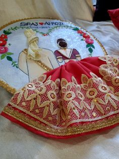 a red and gold sari laying on top of a white bed next to a pillow