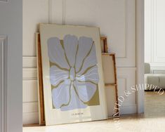 a white flower is sitting on the floor in front of a framed art print that reads la merque