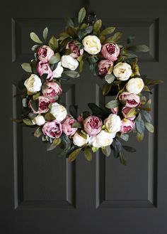 a wreath with pink and white flowers hanging from the front door on a black door