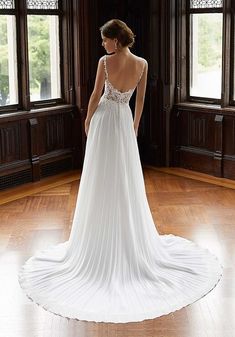 a woman in a white wedding dress standing on a wooden floor looking out the window