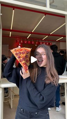 a woman holding up a slice of pizza in front of her face and making a funny face