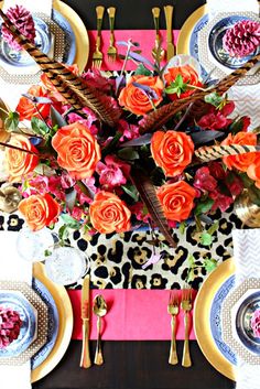 the table is set with plates, silverware and colorful flowers on it's centerpiece