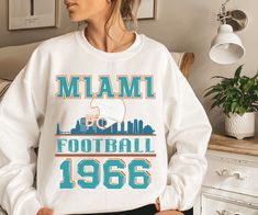 Are you ready for FOOTBALL SEASON?! And are you looking for a unique, retro design that differs from the generic NFL team gear you find elsewhere online? This vintage styled, cute Miami Football sweatshirt is perfect to support your Miami Dolphins this football season! This crewneck is available in white, ash grey, sport grey, heather grey, sand, and black (pick one up for your husband/boyfriend/best friend/dad/mom etc too!) Sweatshirt details are below, and the models in the pictures are wearin Miami Dolphins Sweatshirt, Retro Miami, Nfl Sweatshirt, Miami Football, Boyfriend Best Friend, Vintage Miami, Nfl Miami Dolphins, Football Sweatshirt, Team Gear