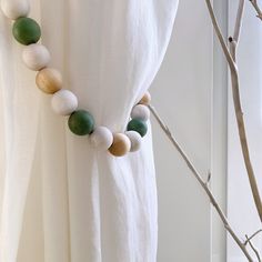 a white curtain with some green beads hanging from it's side next to a tree branch