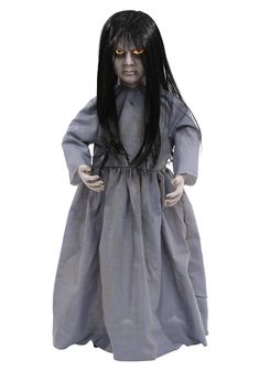 a creepy doll with long black hair wearing a gray dress and orange eyes, standing in front of a white background