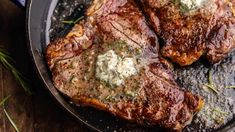 two steaks in a skillet with herbs on the side and butter on top