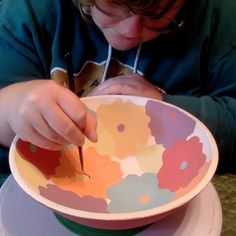 a young boy is cutting paper into a flowered bowl with scissors and glue on it