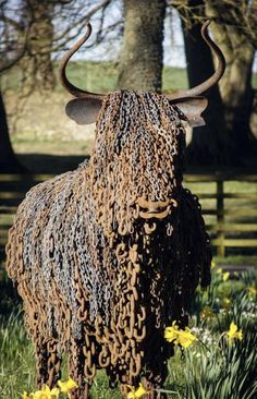 an animal made out of chains standing in the grass with trees and flowers behind it