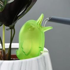 a green plastic bird sitting in a white vase next to a black and gray plant