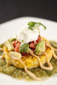 a white plate topped with an enchilada covered in sour cream and avocado