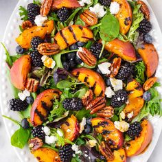 a salad with peaches, blackberries and pecans on a white platter