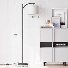 the floor lamp is next to a white cabinet with drawers and pictures on it,