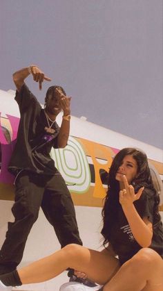 a man and woman sitting on the ground next to an airplane with their hands up