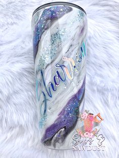 this tumble is decorated with glitter and hand painted mermaids on the side, while it sits on a white furnishing