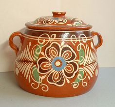 a brown and blue pot with flowers painted on the side is sitting against a white wall