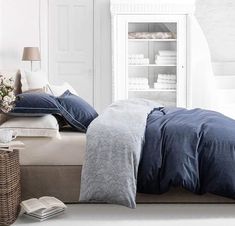 a bed with blue sheets and pillows in a room next to a book shelf filled with books