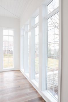 an empty room with large windows and hard wood flooring on the side of it