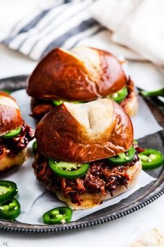 three pulled pork sliders with jalapenos on a black and white plate