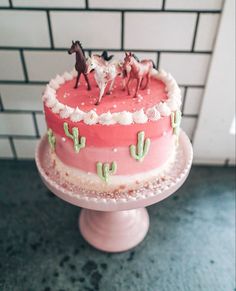 there is a cake with horses on top and cactus in the middle, sitting on a pedestal