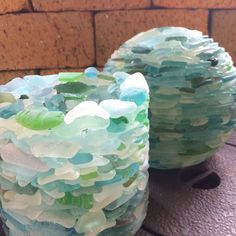 two vases made out of sea glass sitting on a table next to a brick wall