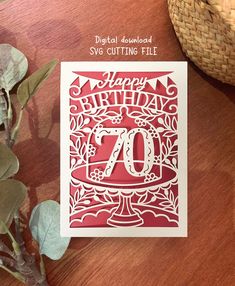 a red and white birthday card with the number seventy on it next to some plants