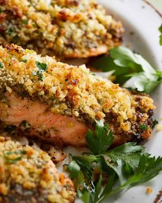 two pieces of meat covered in parmesan and garnished with herbs on a white plate