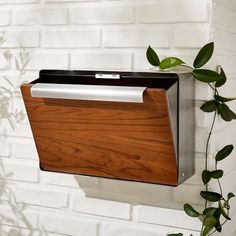 a metal and wood folder holder hanging on a white brick wall next to a green plant