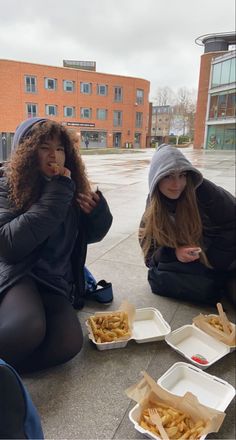 two women sitting on the ground eating french fries