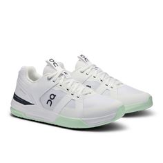 a pair of white sneakers with green accents on the soles and an upper lace